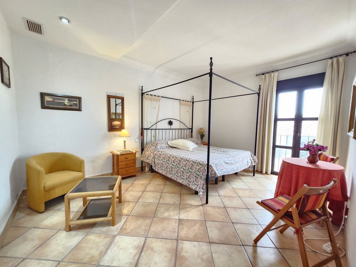 A bedroom with a four-poster bed, armchair, coffee table, and a small dining table by the window with a balcony view.
