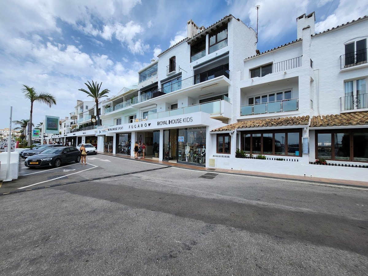 Street view of a white commercial building with shops and apartments above, palm trees, and cars parked on the street.