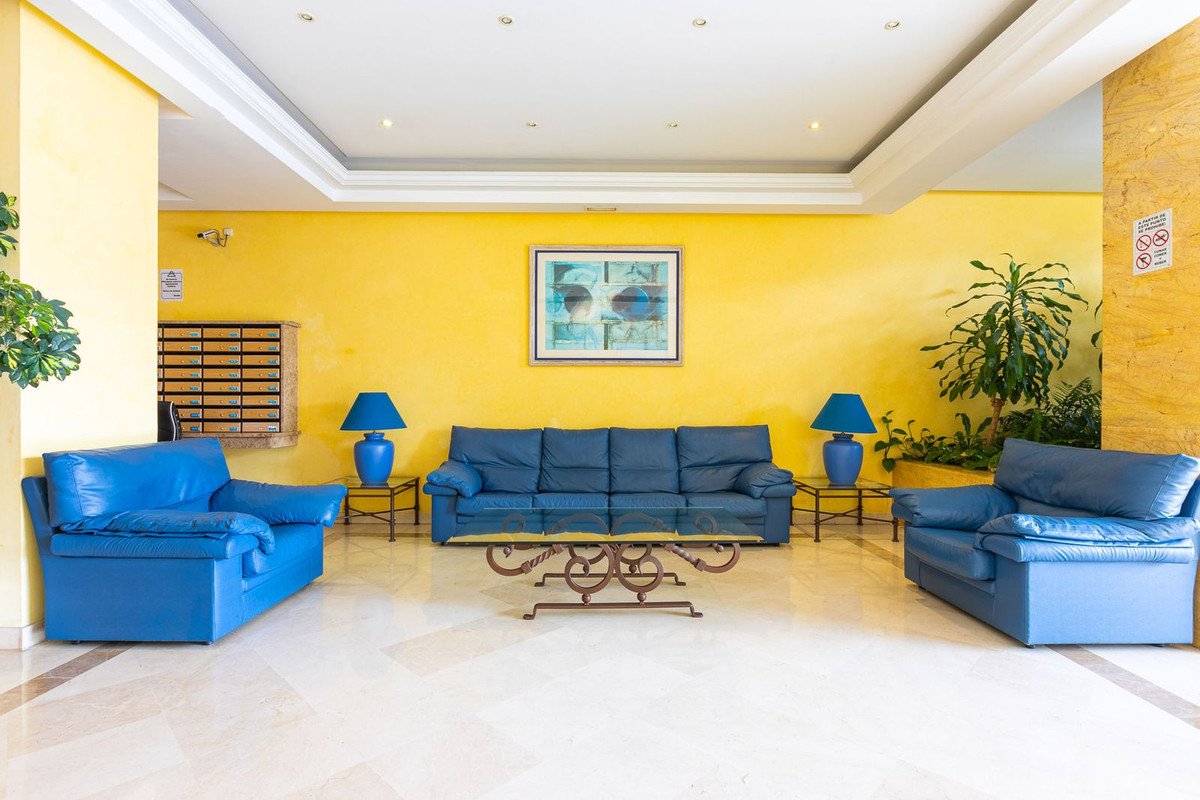 A bright living room with yellow walls, blue leather sofas, a glass coffee table, and two blue table lamps.
