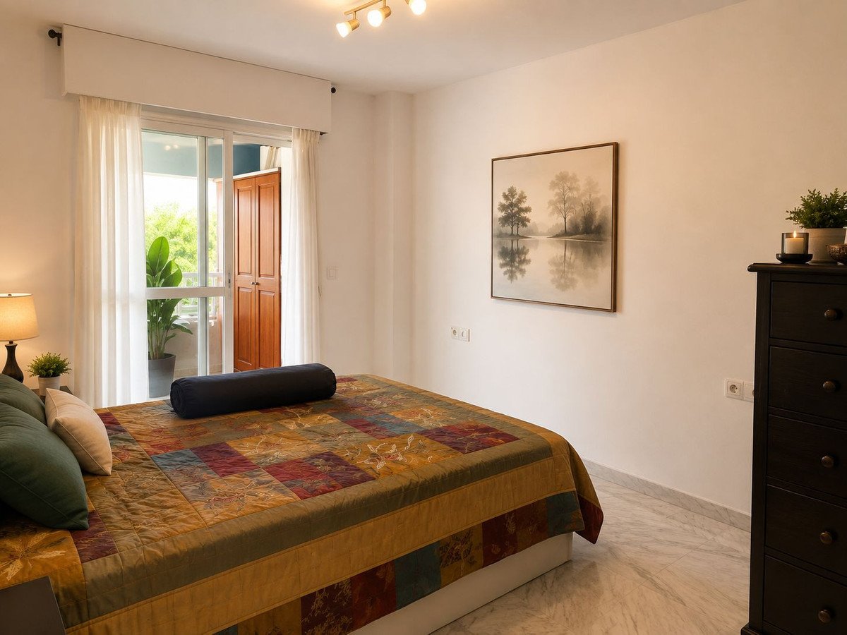 Bedroom with a colorful quilt on the bed, a dresser, and a door leading to a balcony with plants.