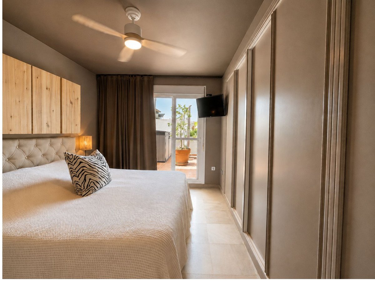 A bedroom with a large bed, a TV mounted on the wall, and sliding glass doors leading to a balcony.