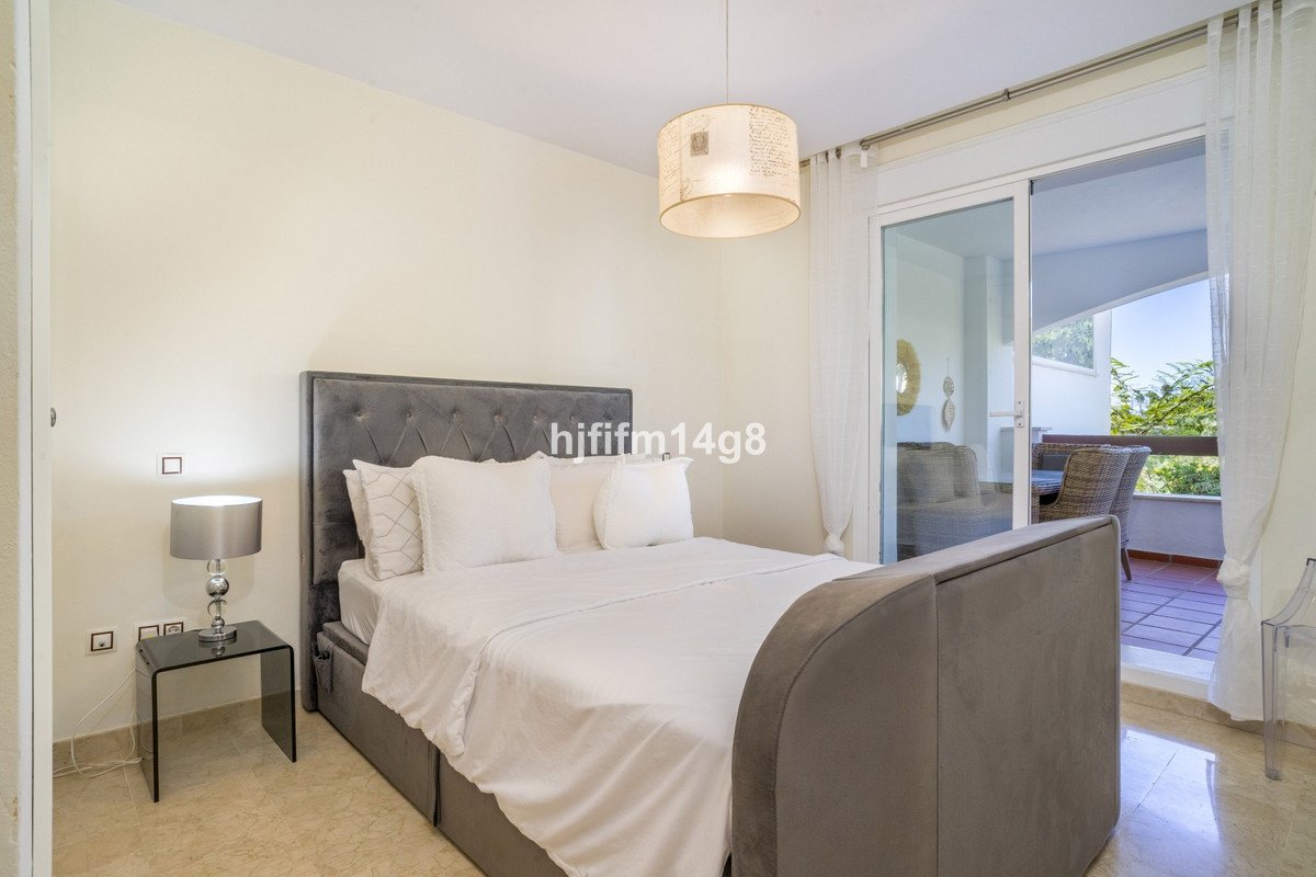 A plush grey bed with white linens in a bedroom, featuring a glass door leading to a balcony with outdoor seating.