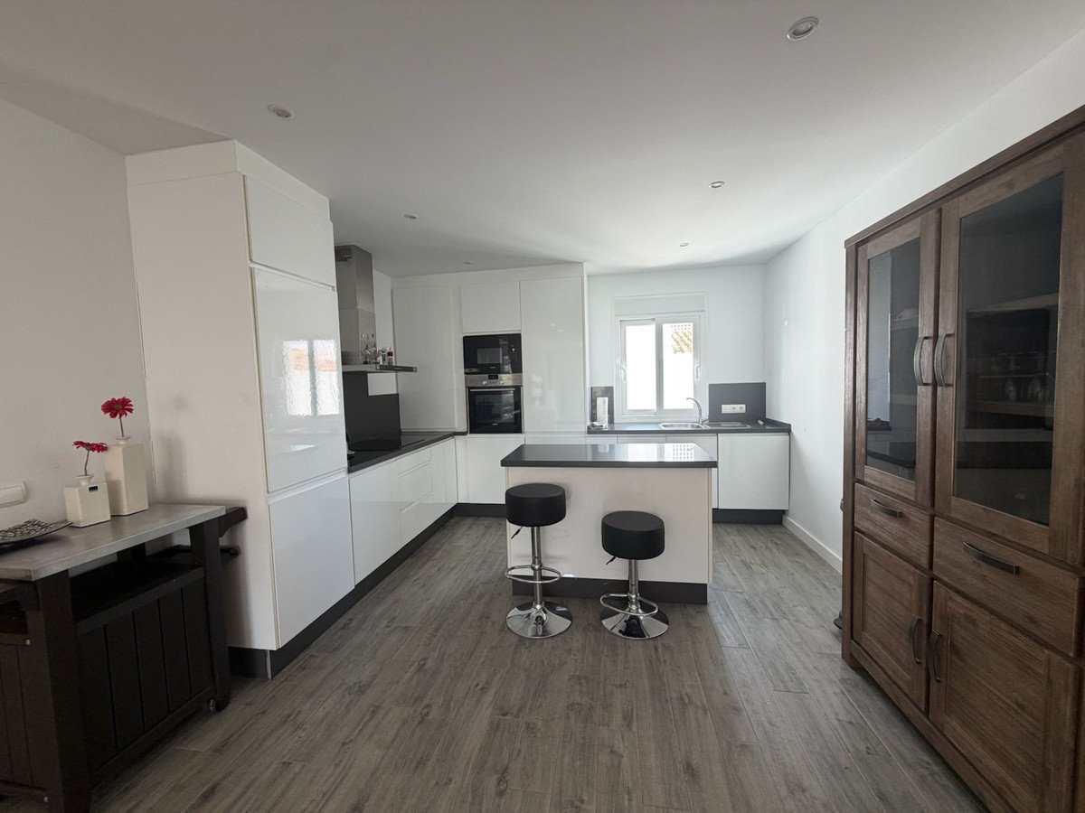 Modern white kitchen with a central island, sleek cabinetry, and a wooden display cabinet.