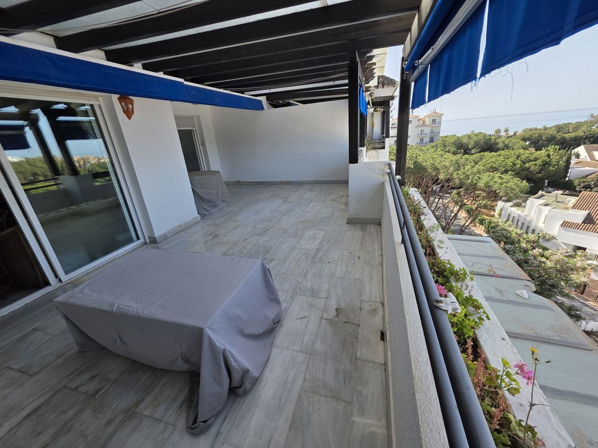A spacious terrace with large sliding doors, covered furniture, and a view of trees and distant buildings.
