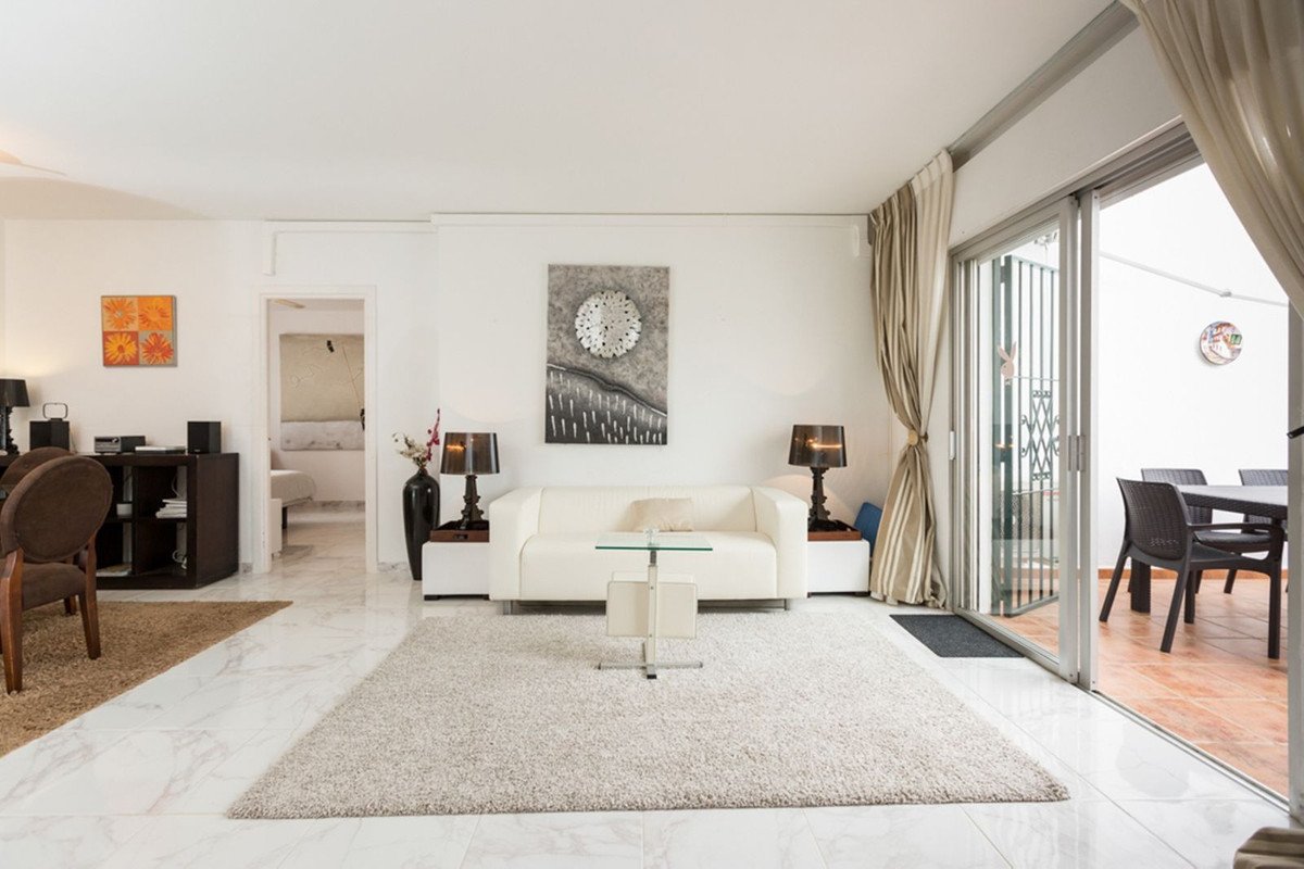 Modern living room with white sofa, large rug, and sliding doors opening to an outdoor dining area with a table and chairs.