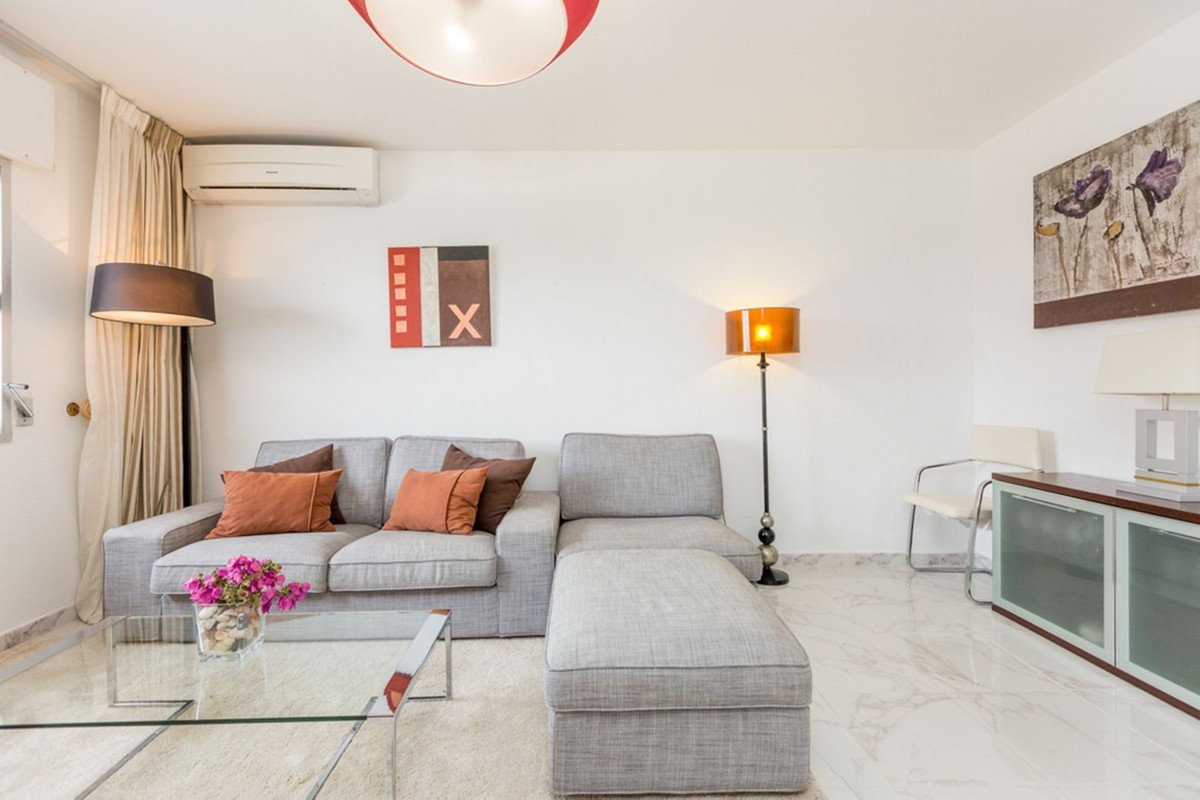 A modern gray sectional sofa with orange and brown pillows sits in a bright living room with a glass coffee table and floor lamps.