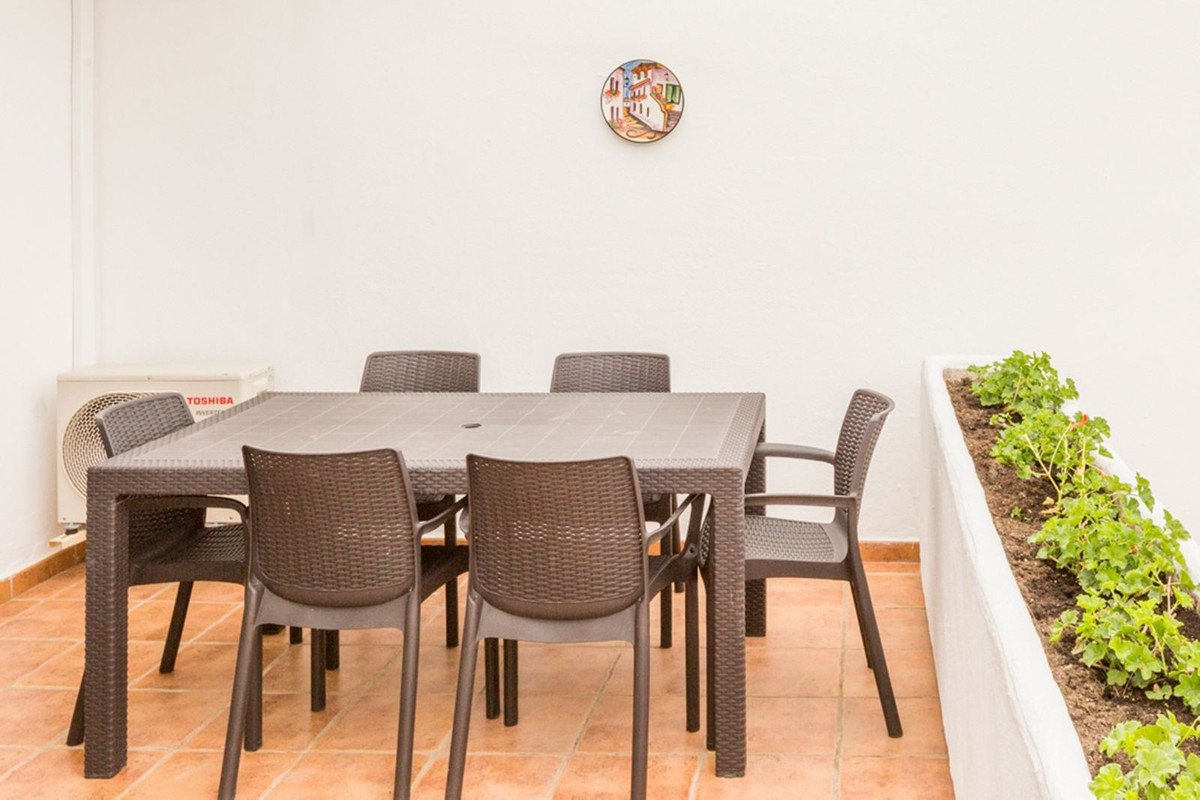 Outdoor terrace with a table and chairs set for dining, next to a white planter box with green plants.
