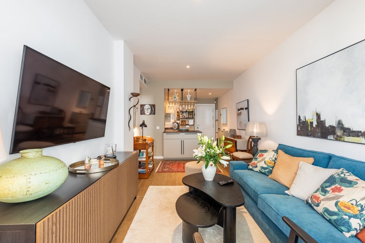 Modern living area with a blue sofa, coffee table, and a view of a kitchenette with a bar area.