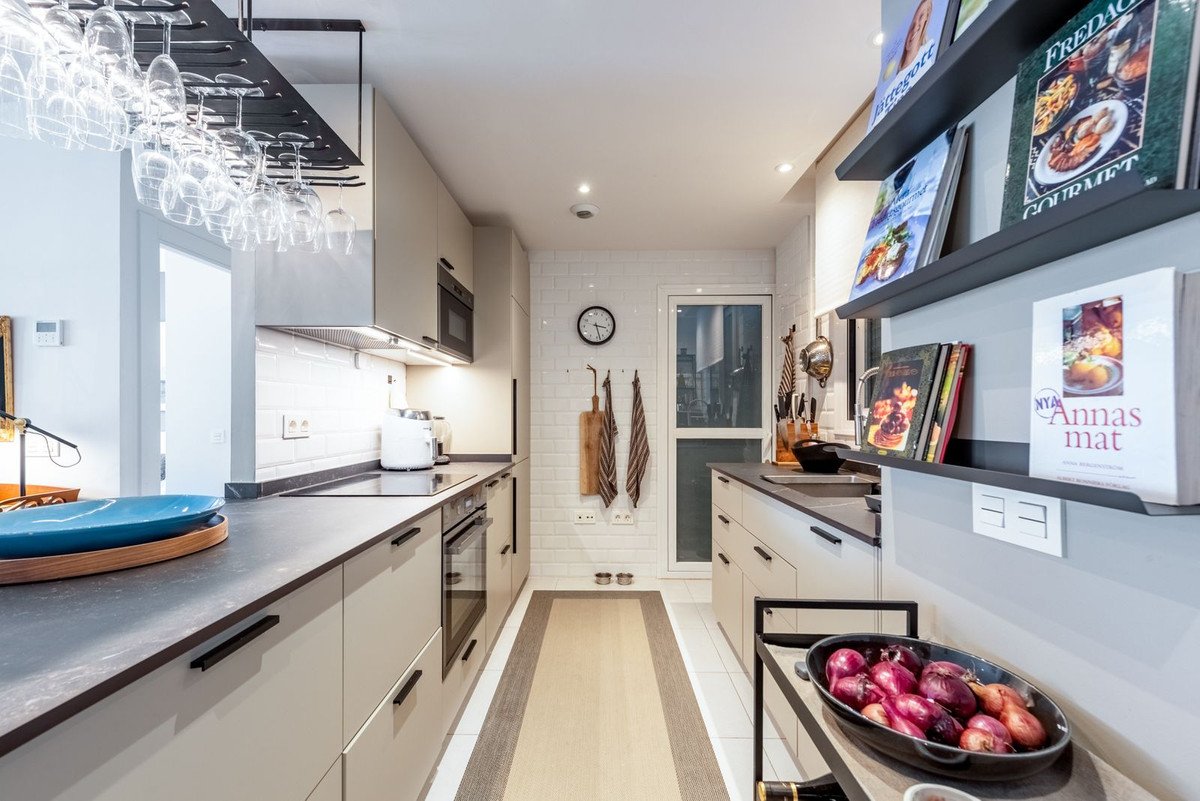 A modern, long kitchen with ample counter space, wine glass rack, and subway tile backsplash.