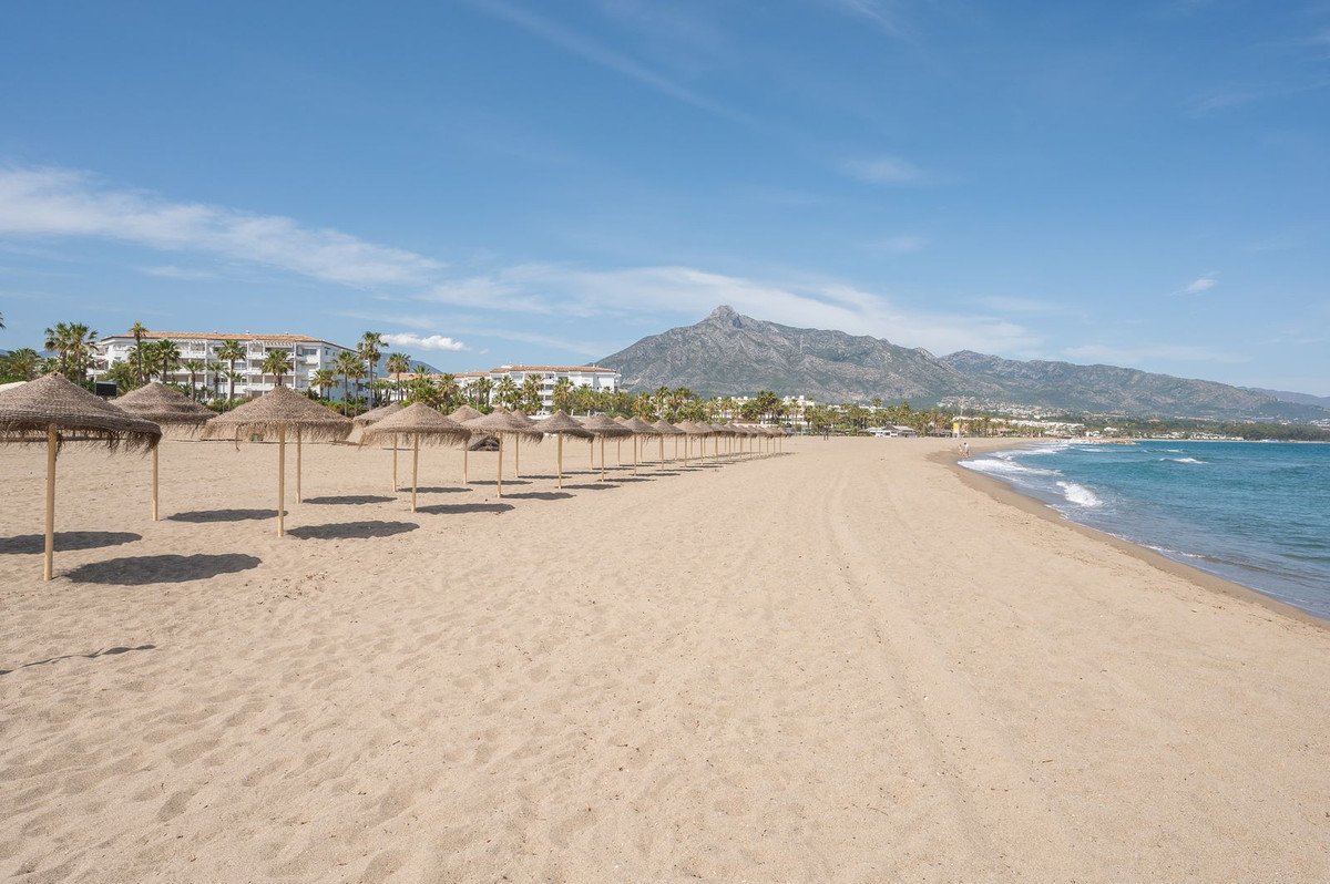 Sandy beach with thatched umbrellas, ocean waves, and mountain backdrop