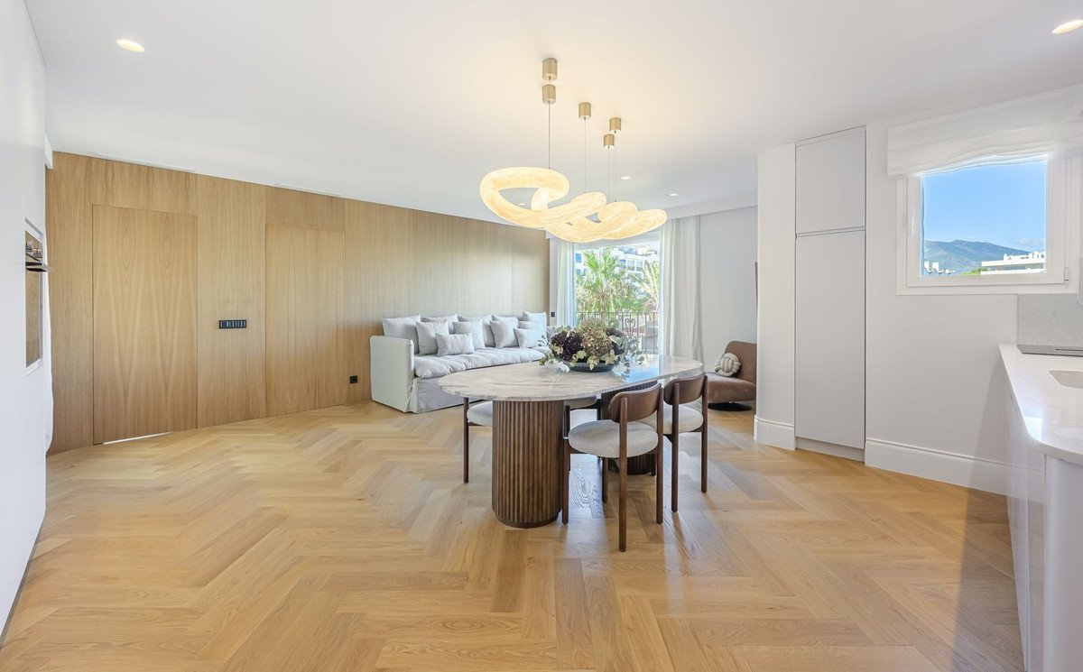Modern open-plan living and dining area with herringbone wood floors, contemporary lighting, and large windows