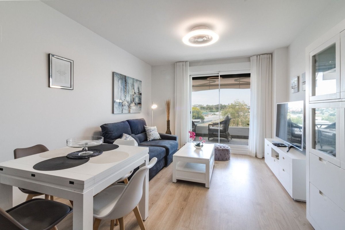 Modern living and dining area with blue sofa, white table, and balcony access offering a garden view.