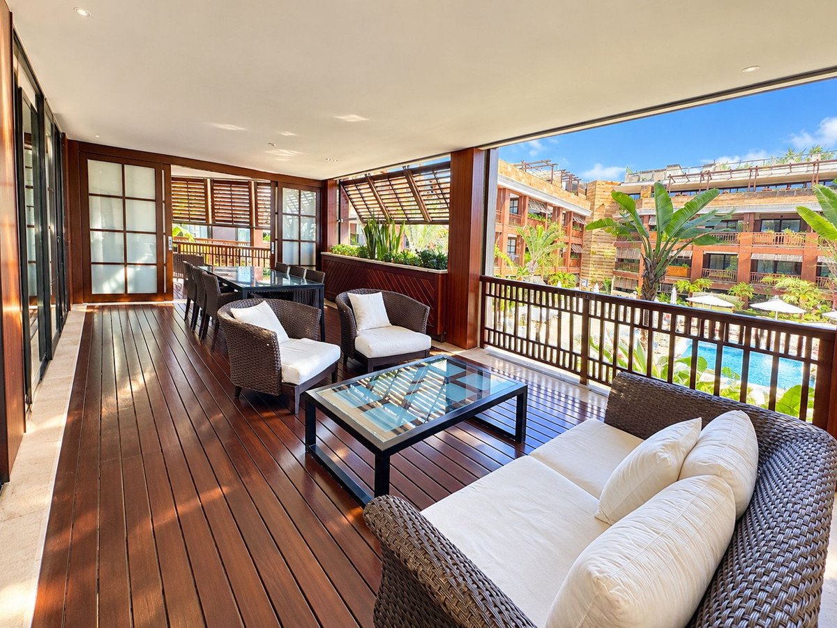 Spacious outdoor living area with wicker furniture, wooden deck, and pool view.
