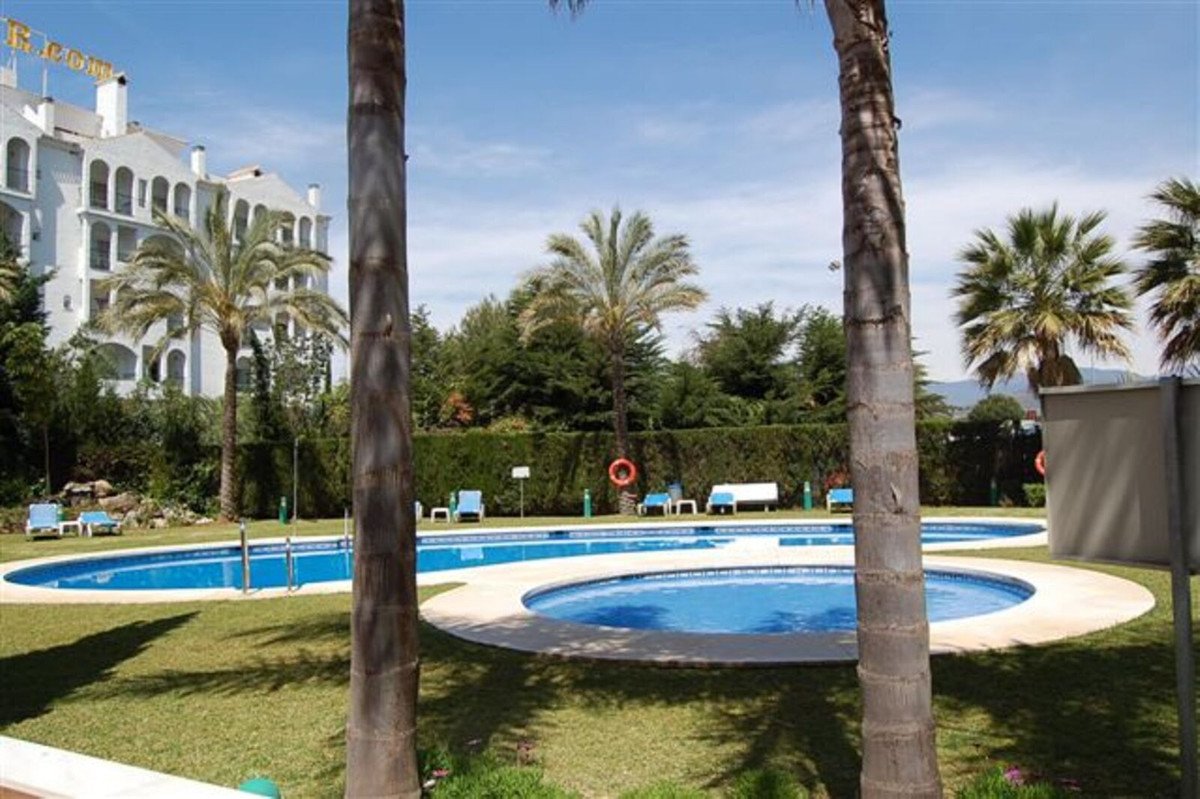 Outdoor swimming pools with lounge chairs and palm trees, overlooking a white resort building.