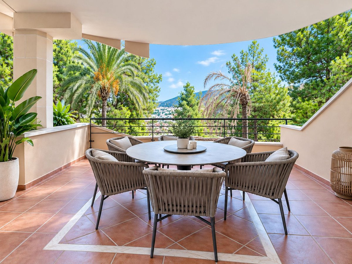 A covered terrace with a dining set and chairs, offering a view of lush greenery and distant town.