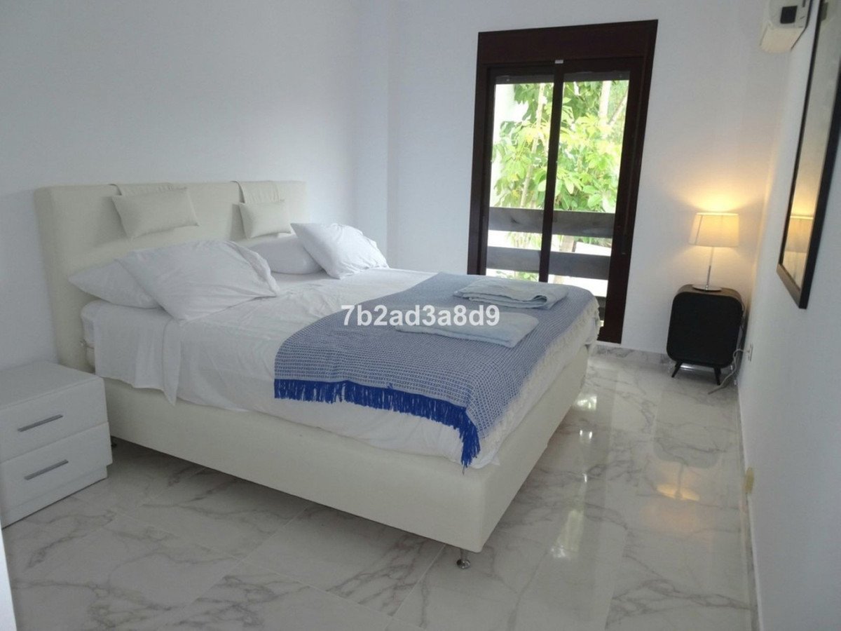 A bright bedroom with a white bed, marble floor, and a view of greenery through a glass door.