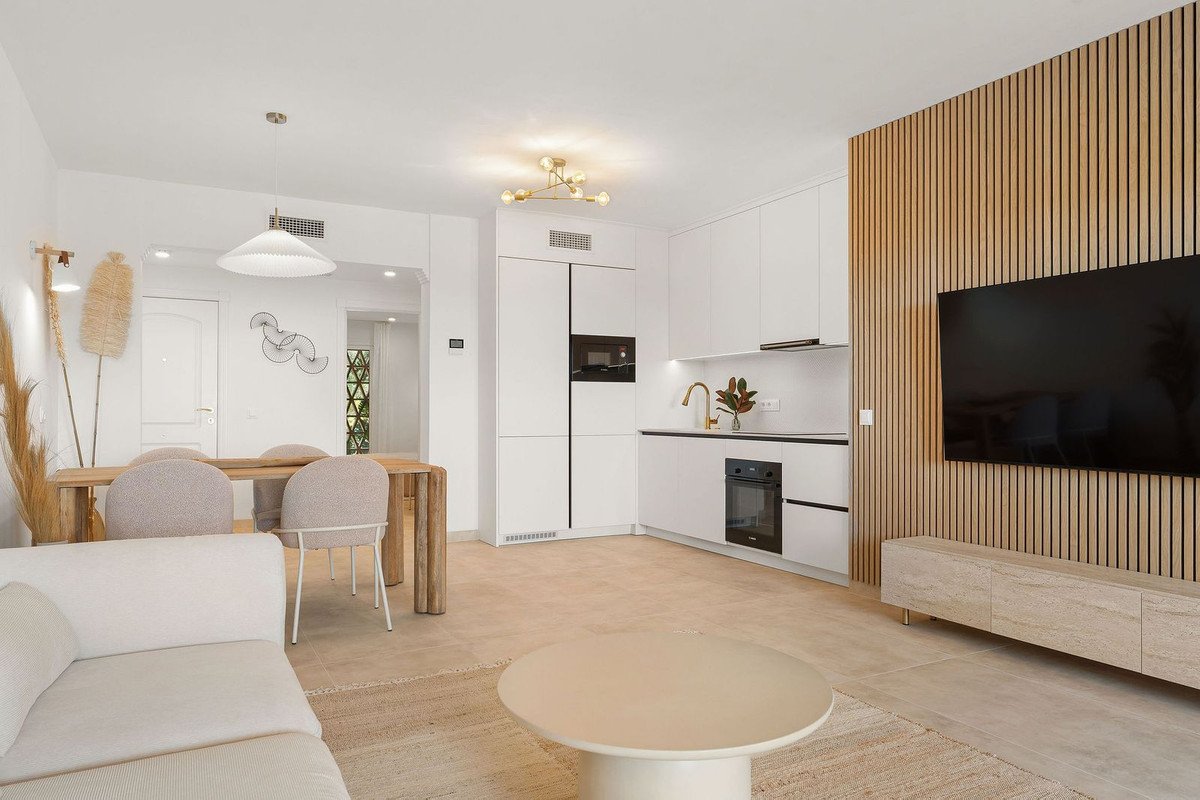 Open-plan living area with modern kitchen, dining table, sofa, and TV on a slatted wooden wall.
