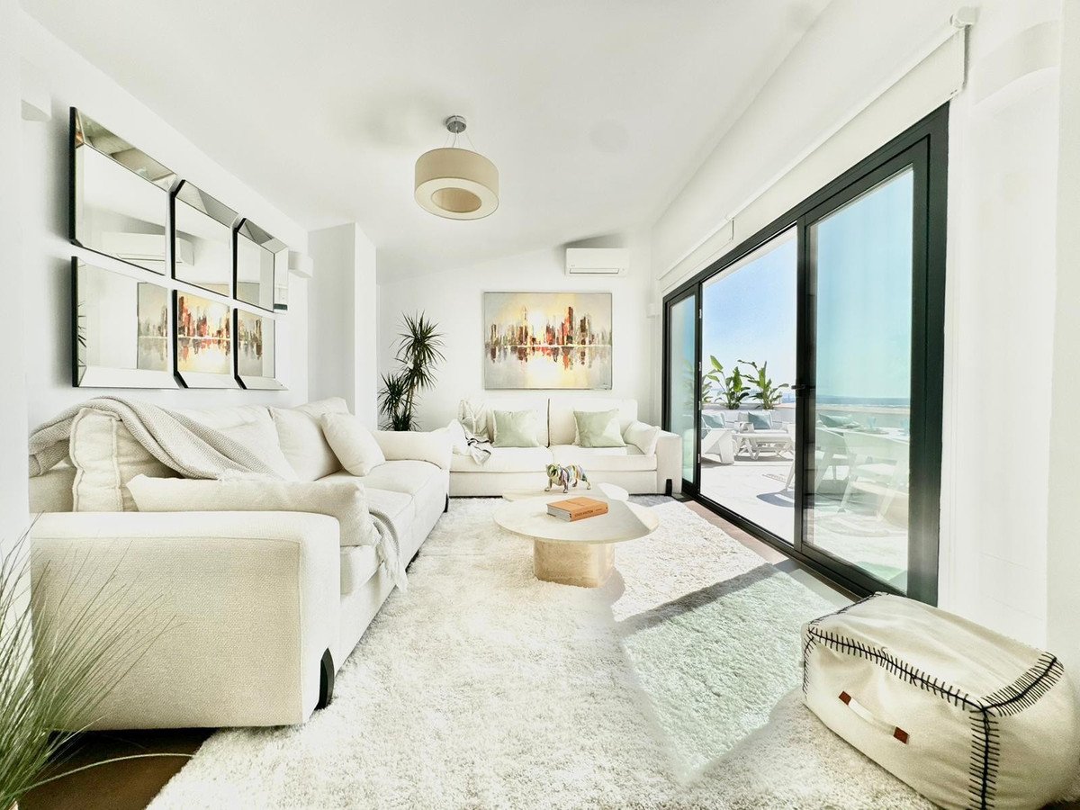 Bright living room with white sofas, large windows, and a sea view terrace with outdoor seating. Modern decor.