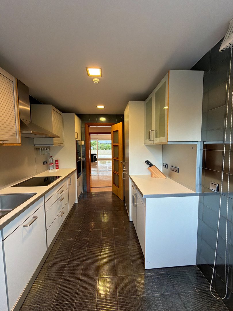 A modern galley kitchen with white cabinets, stainless steel appliances, and a view through the open doorway.