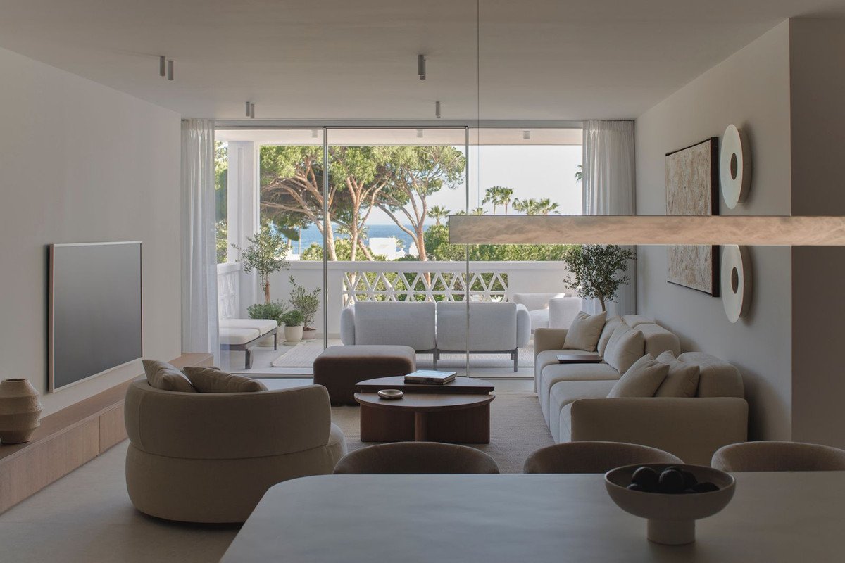 Modern living room with comfortable sofas, balcony access, and a view of trees and the sea.