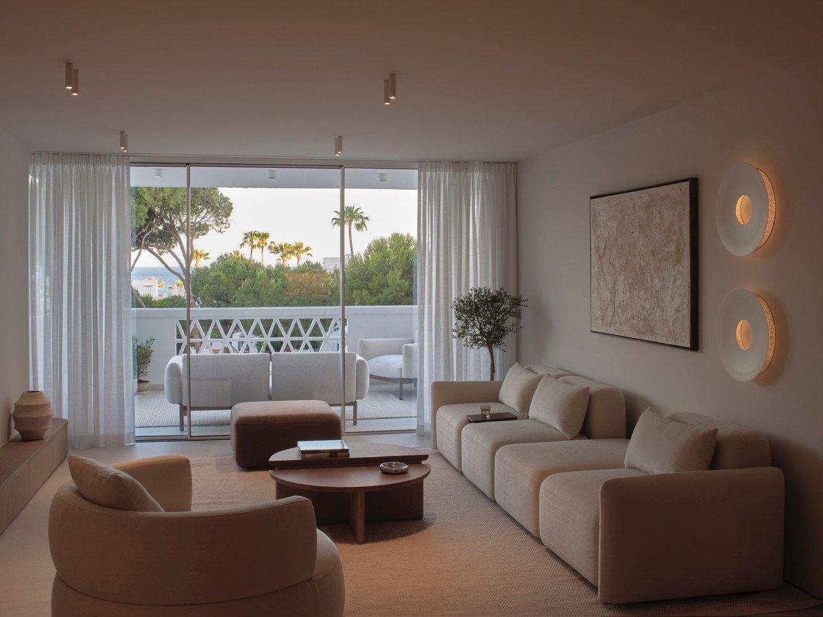 Modern living room with large sectional sofa, view of a balcony with sea and palm trees.