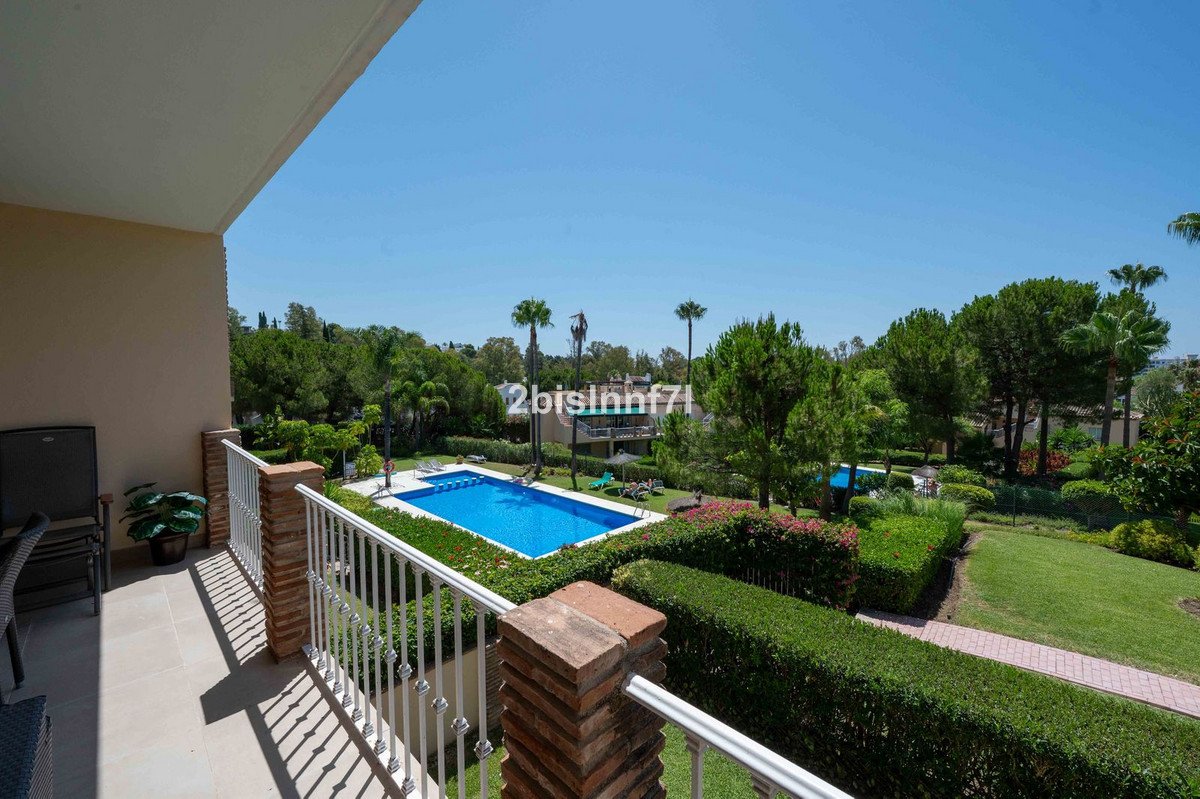Balcony overlooking a swimming pool and lush garden with palm trees on a sunny day.
