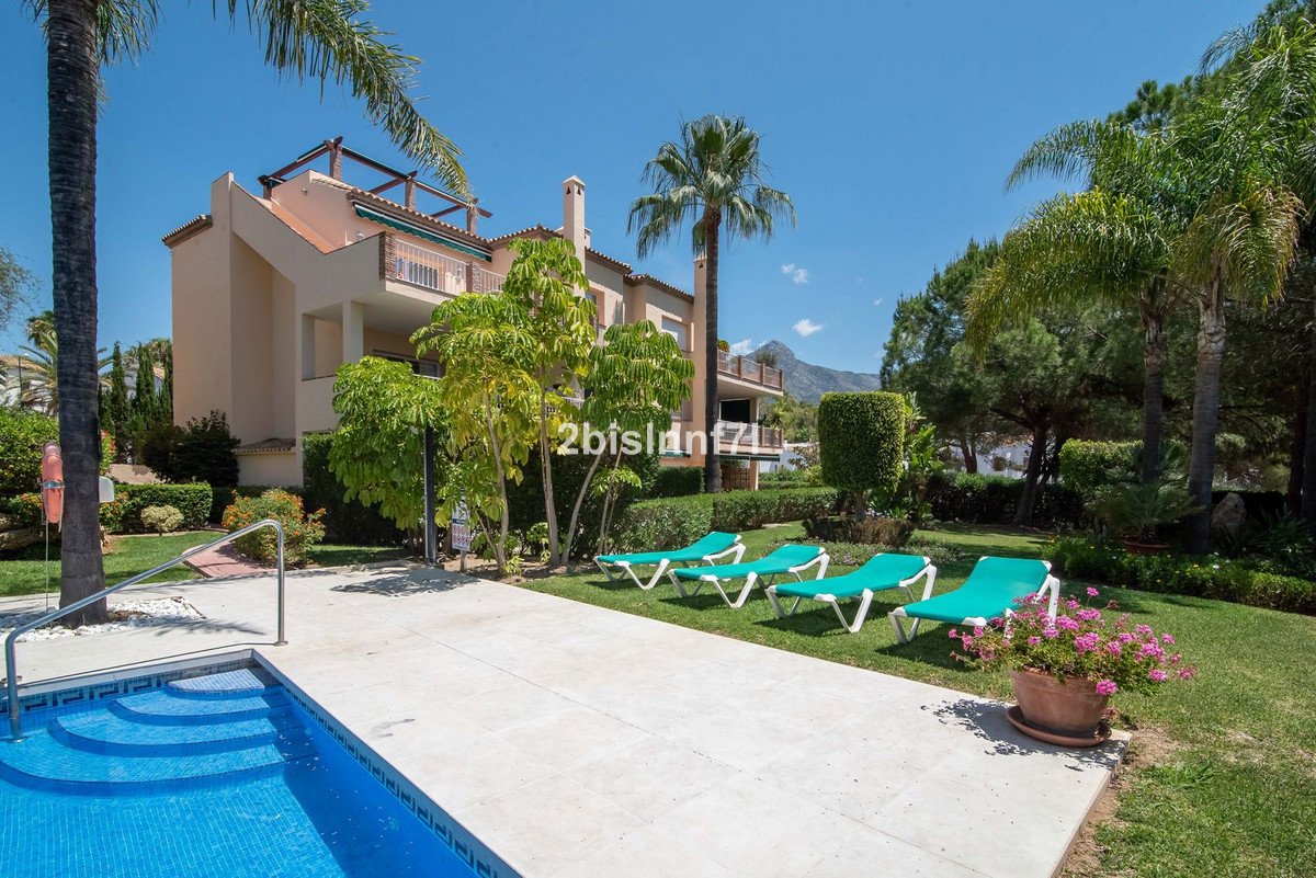 A swimming pool with lounge chairs on the terrace, lush greenery, and mountains in the background under a clear blue sky.