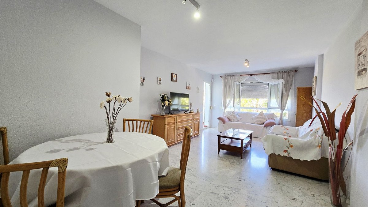 A dining area and living room with a sofa, coffee table, and TV stand, featuring a large window with natural light.