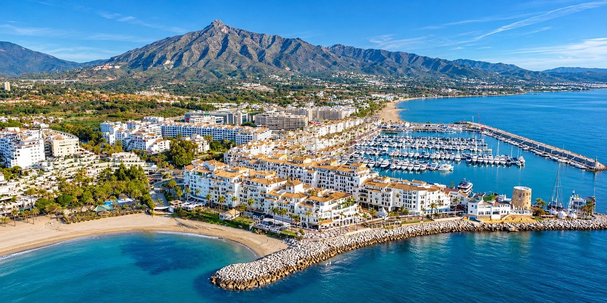 Aerial view of a coastal town with marina, beach, and mountain backdrop