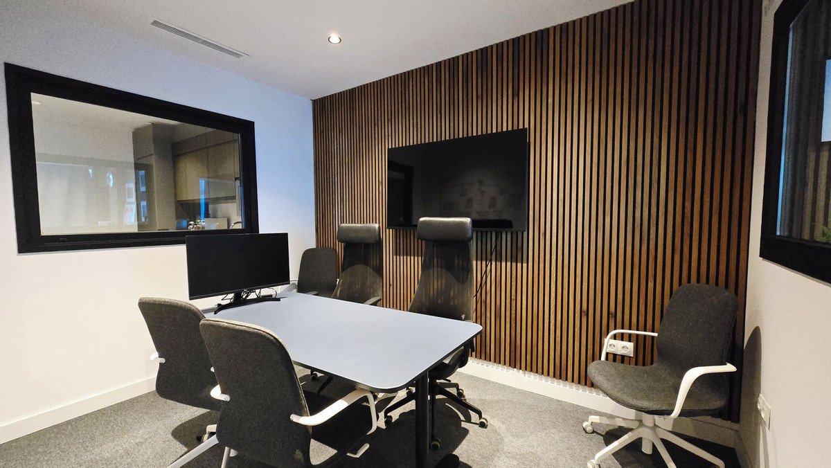 Modern conference room with a large screen, sleek table, ergonomic chairs, and wood-paneled wall.