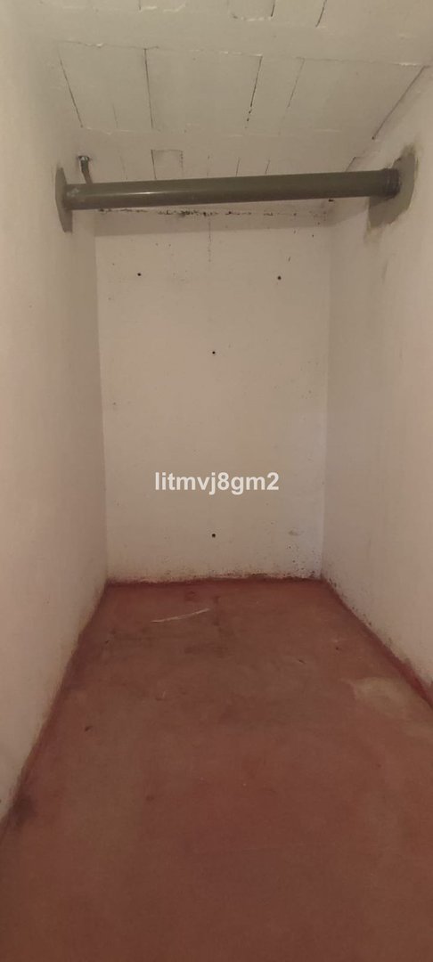 Empty interior storage closet with a metal pipe mounted on the wall and ceiling. Features white walls and a red floor.