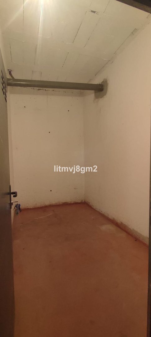 Empty storage room with bare walls, a pipe along the ceiling, and a brown floor.