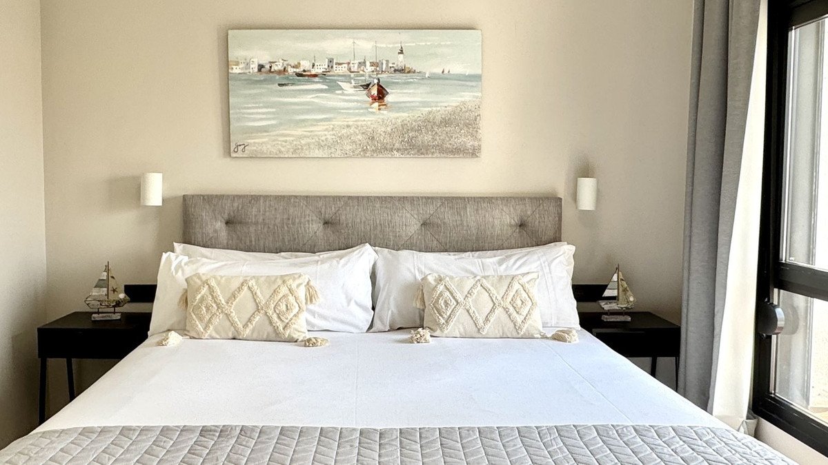 A cozy bedroom with a large bed, nautical decor, and a coastal painting above the headboard.