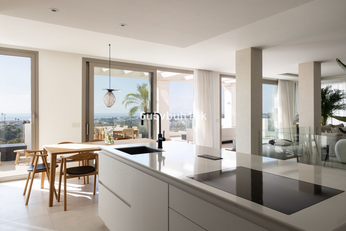Modern kitchen island with sink and induction hob, overlooking a dining area and a terrace with sea and palm tree views.