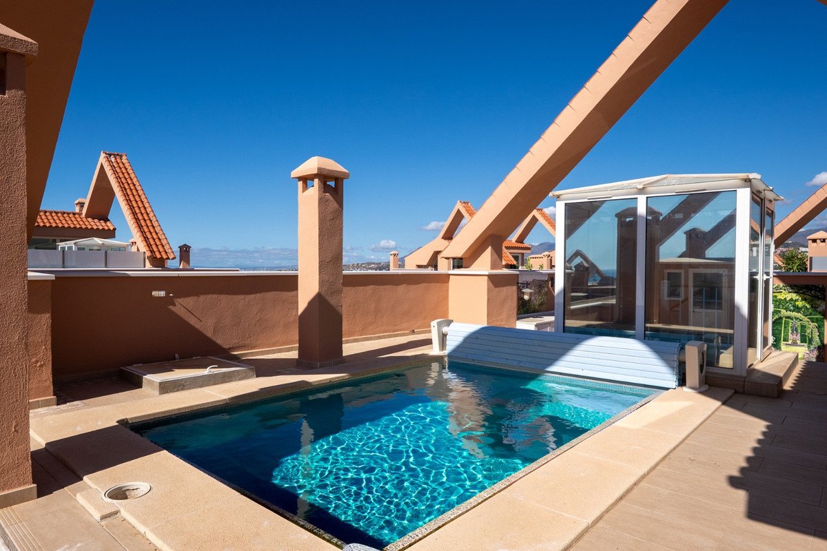 A private terrace features a small swimming pool with a retractable cover and a glass enclosure, overlooking a distant coastline under a clear blue sky.