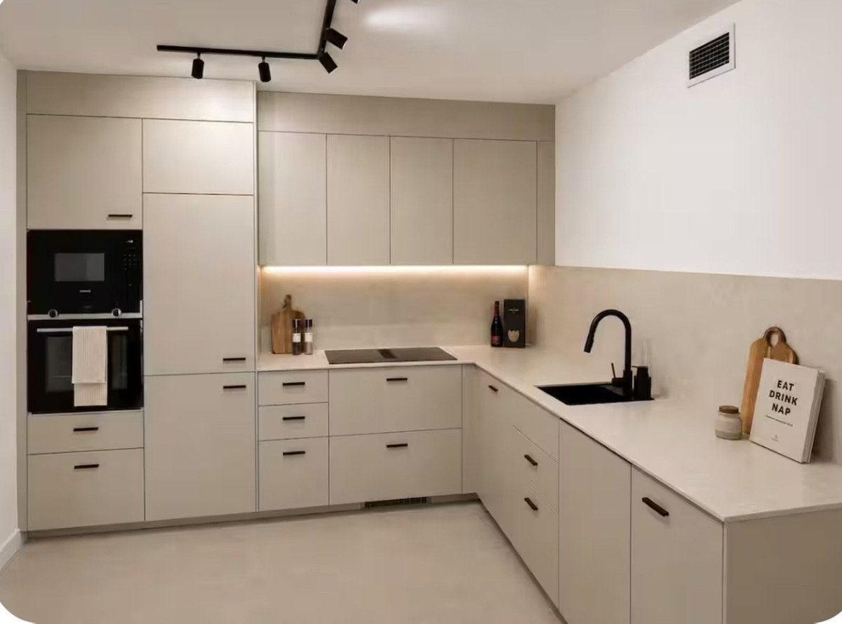 Modern L-shaped kitchen with light beige cabinets, built-in oven and microwave, black sink, and induction hob.