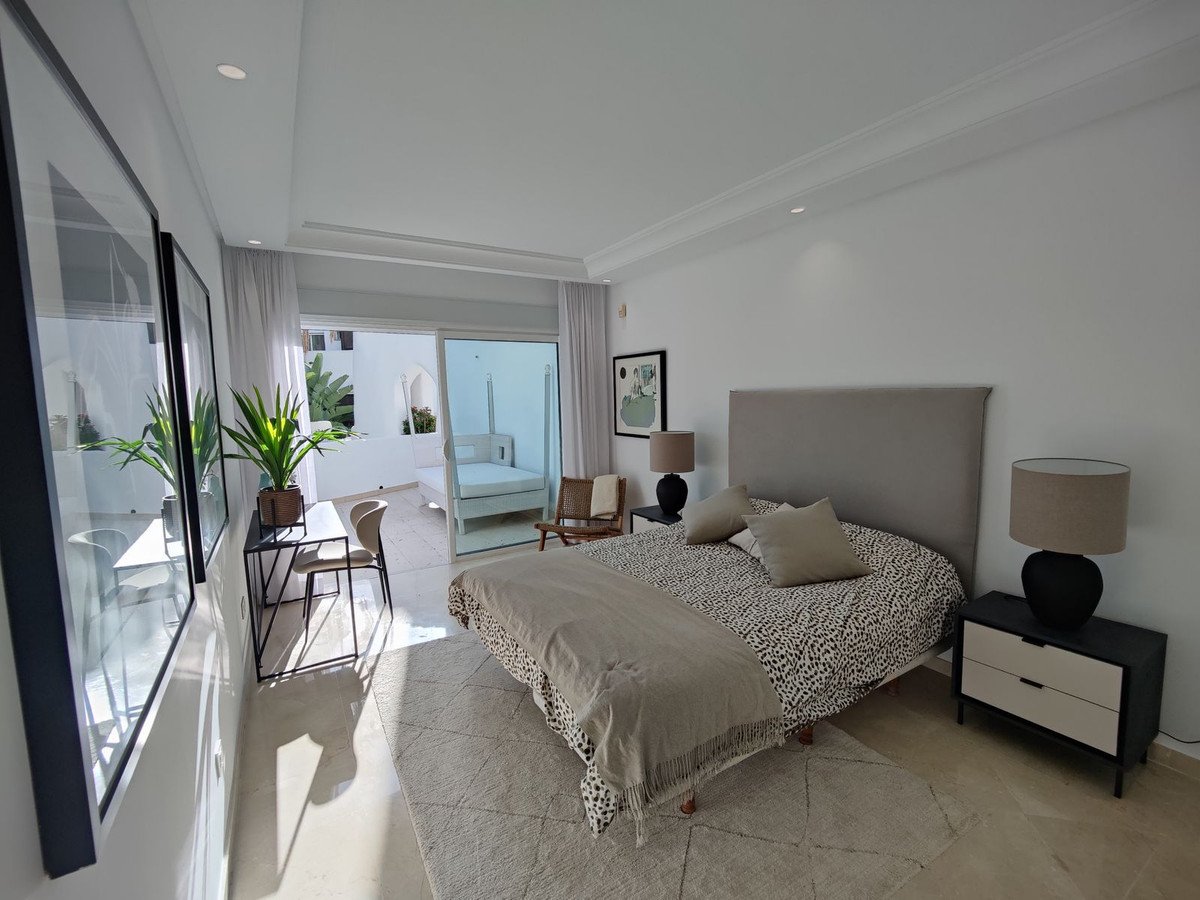 Modern bedroom with a king-size bed, bedside tables, desk, balcony access, and a view of an outdoor daybed.