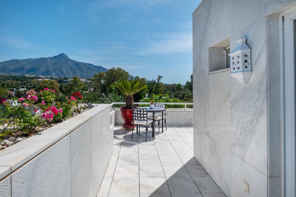 Spacious balcony with marble tiles, table, chairs, and mountain views under a clear blue sky.