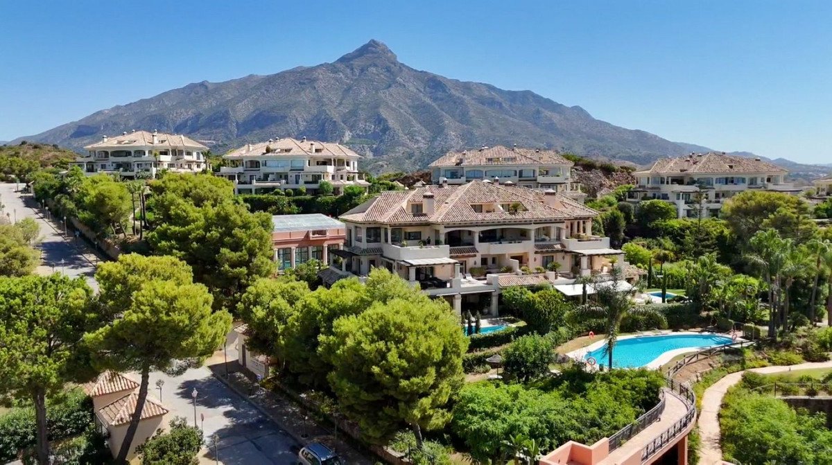 Spacious villas with pools and lush greenery, set against a backdrop of majestic mountains under a clear blue sky.