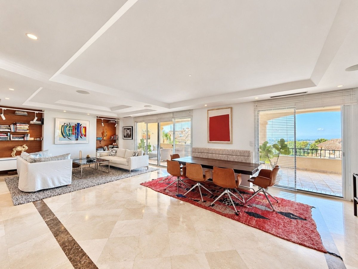 Spacious living and dining area with modern furniture, large windows, and a balcony offering ocean and city views.