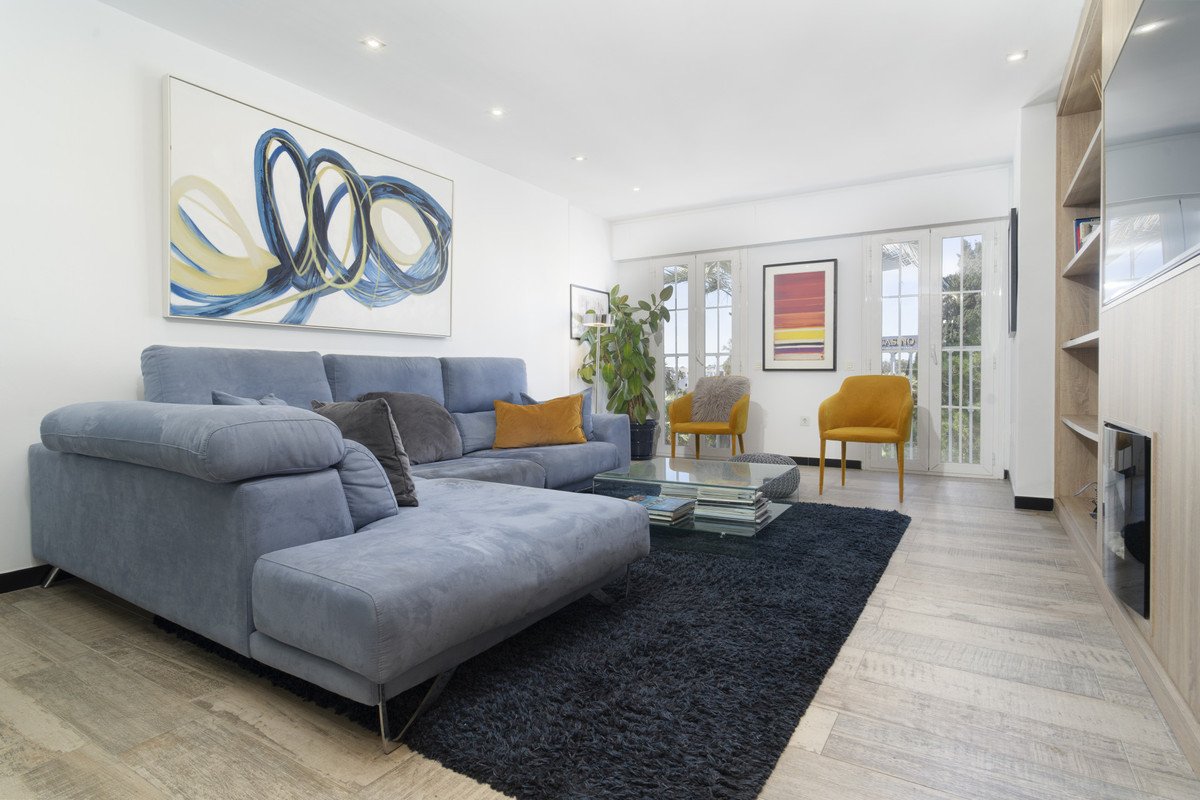 Modern living room with a blue sectional sofa, contemporary artwork, yellow accent chairs, and large glass doors leading outside.