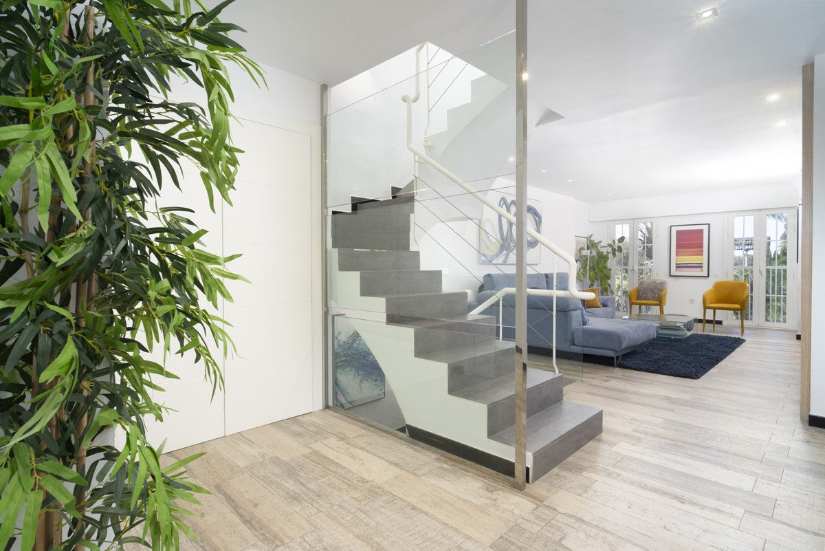 A modern grey staircase with glass railings next to a living area featuring a blue sofa and yellow armchairs.