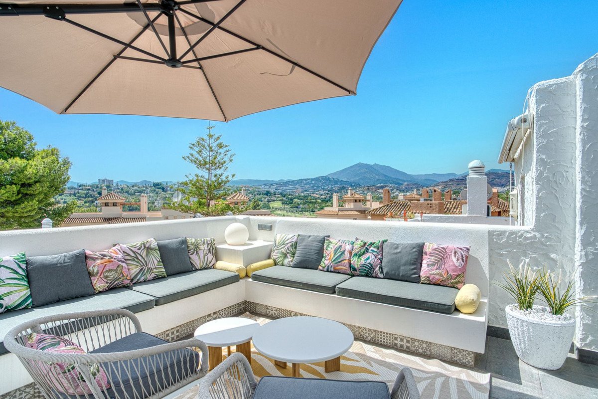 Spacious terrace with built-in seating, comfortable cushions, outdoor furniture, and a stunning mountain view under a large umbrella.