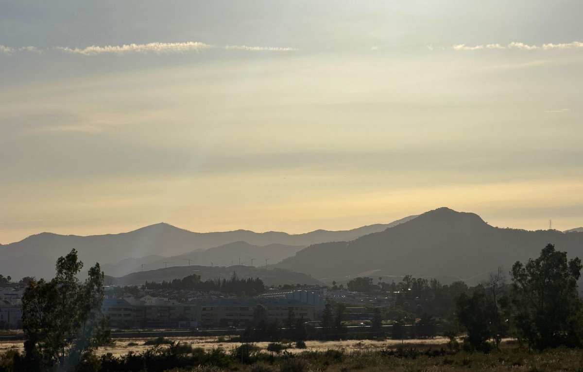 Panoramic view of layered mountains fading into the haze, with a small town and trees in the foreground under a soft sky.