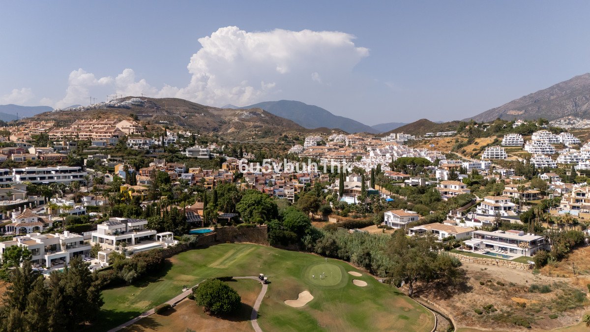 Aerial view of a luxurious villa with a pool, overlooking a golf course and a town with a mountain backdrop.
