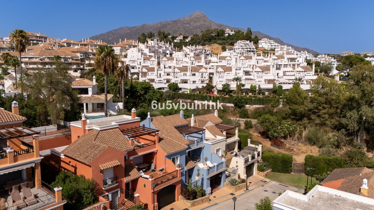 Colorful townhouses with terraces and balconies, overlooking a resort complex and mountains under a clear blue sky.