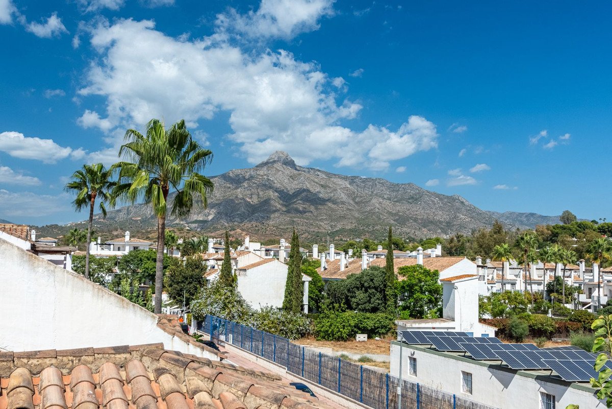 A scenic mountain view overlooking white buildings and palm trees under a blue sky with clouds.