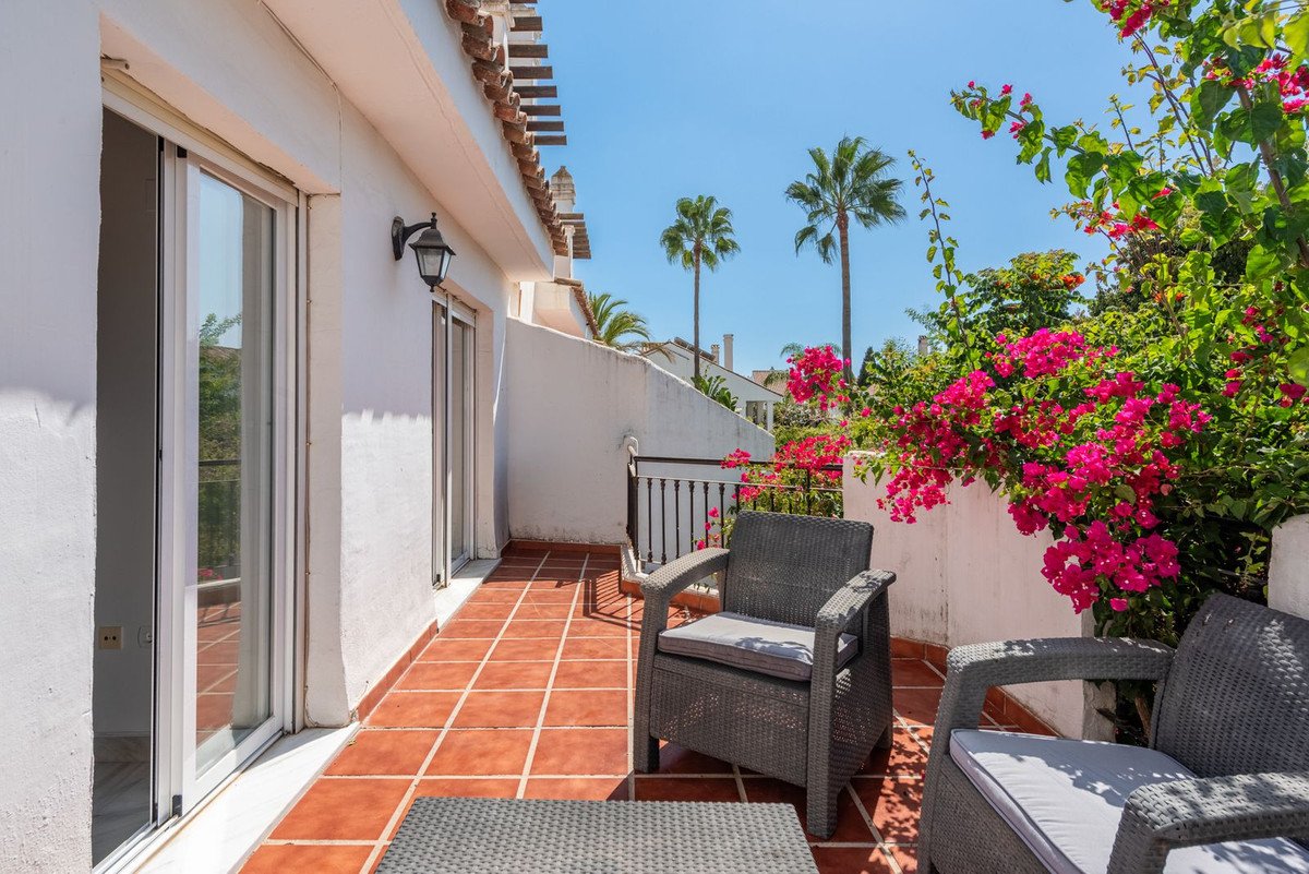 A spacious terrace with comfortable seating, blooming bougainvillea, and palm trees under a clear blue sky.