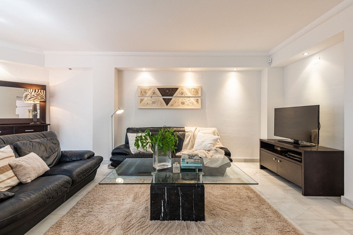 Modern living room with black leather sofas, a glass coffee table, and a television on a stand.