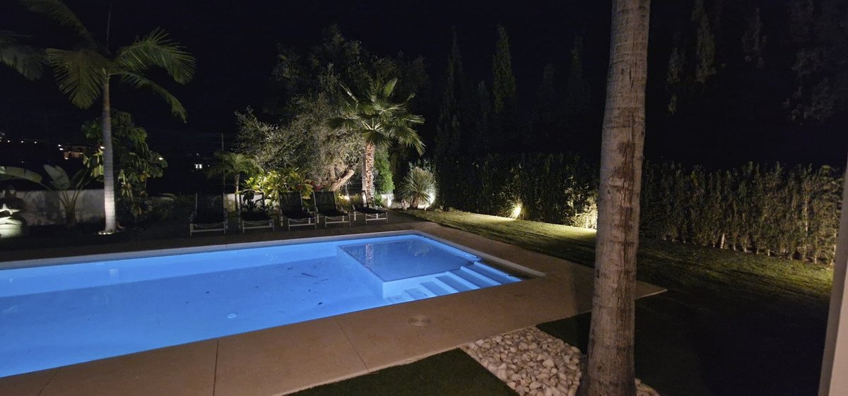 Night time swimming pool with illuminated garden and lounge chairs